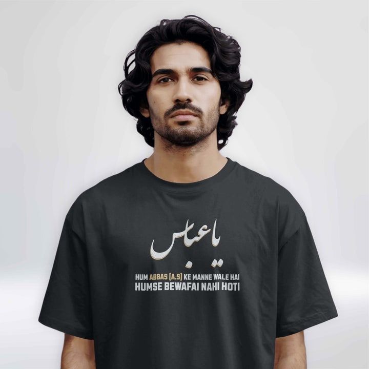 Black Islamic T-shirt with Urdu text "Ya Abbas" and white-yellow bold lettering that says "Hum Abbas (A.S) ke manne wale hai, humse bewafai nahi hoti" on a hanger.

