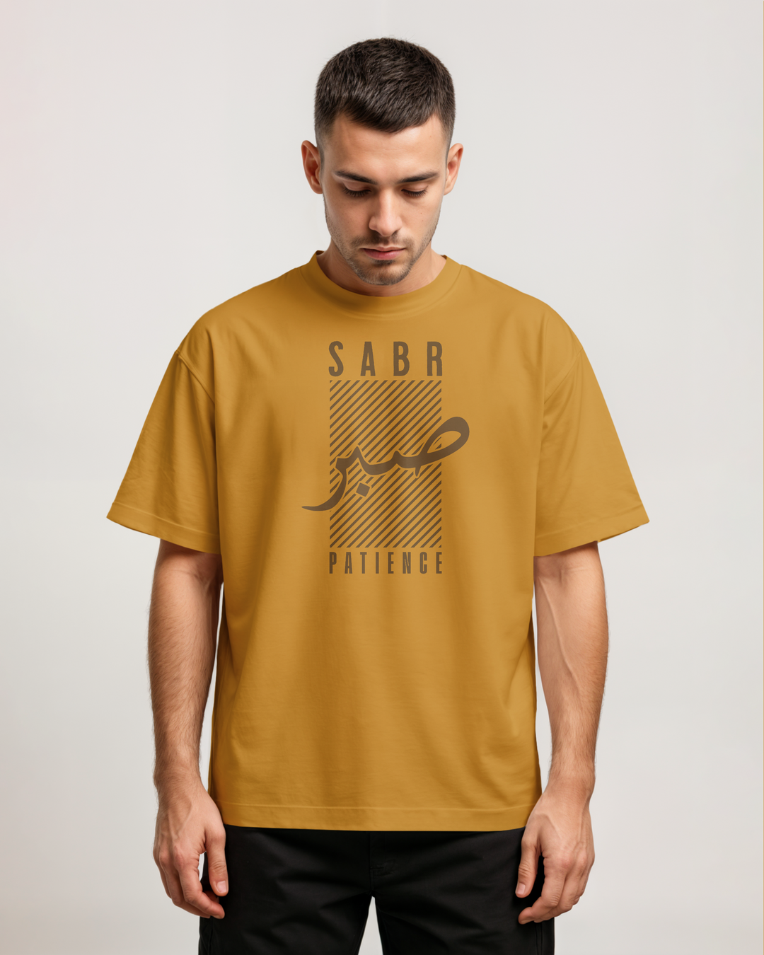 Man wearing a mustard yellow t-shirt with 'Saba' and 'Patience' text on a plain background